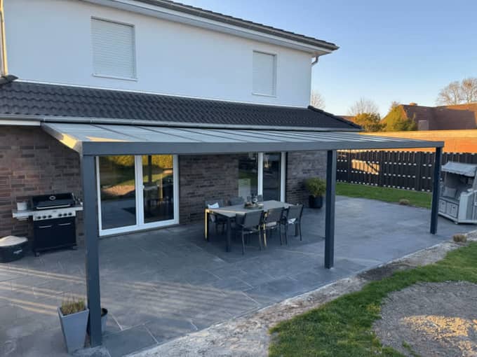 Anthrazitfarbene Basic-Terrassenüberdachung aus Aluminium mit Glasdach über einer Terrasse mit Sitzgruppe – Terravista Sögel