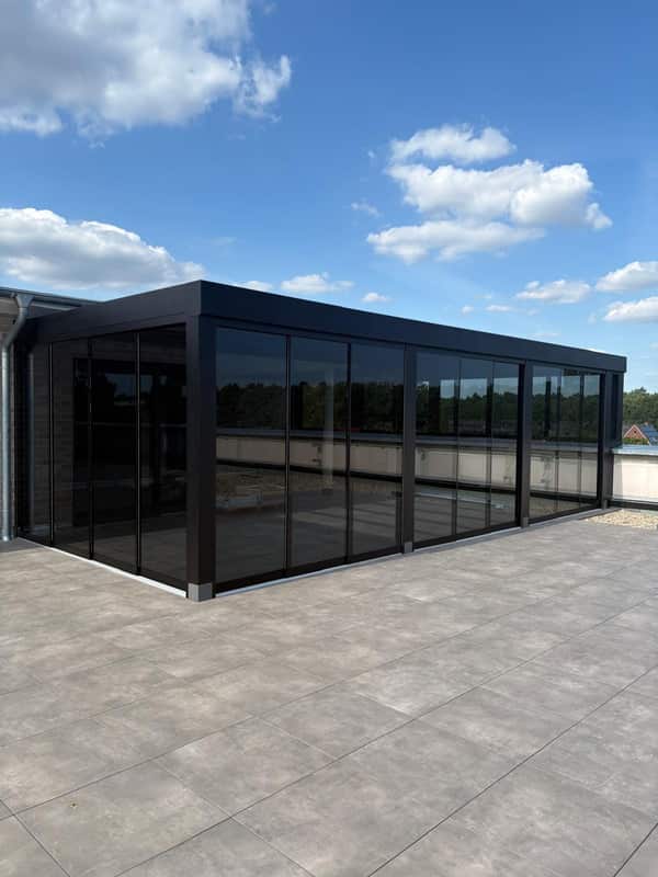 Schwarze Cube-Überdachung mit getönten Glasschiebewänden auf einer Dachterrasse in Lingen