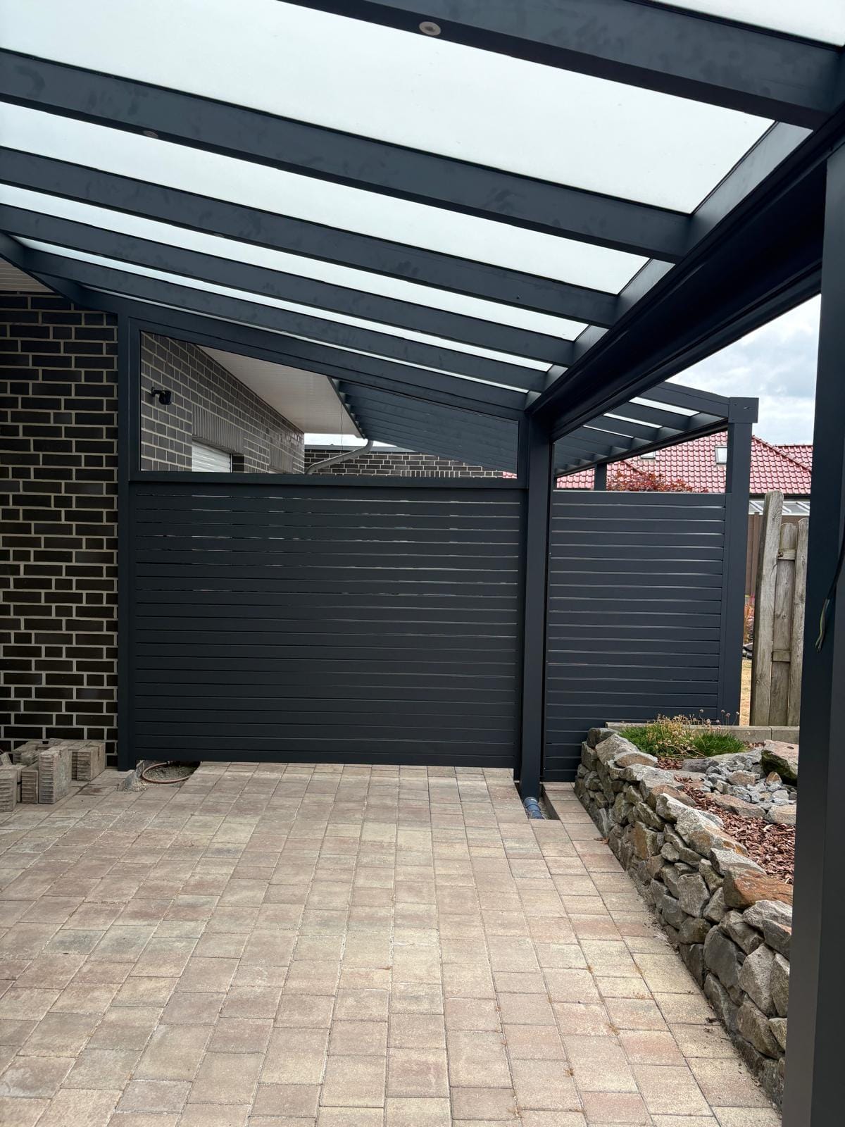 Blick unter eine anthrazitfarbene Basic-Überdachung in Haselünne mit lichtdurchlässiger Dacheindeckung und waagerechtem Aluminium-Lamellen-Sichtschutz zur Nachbarseite