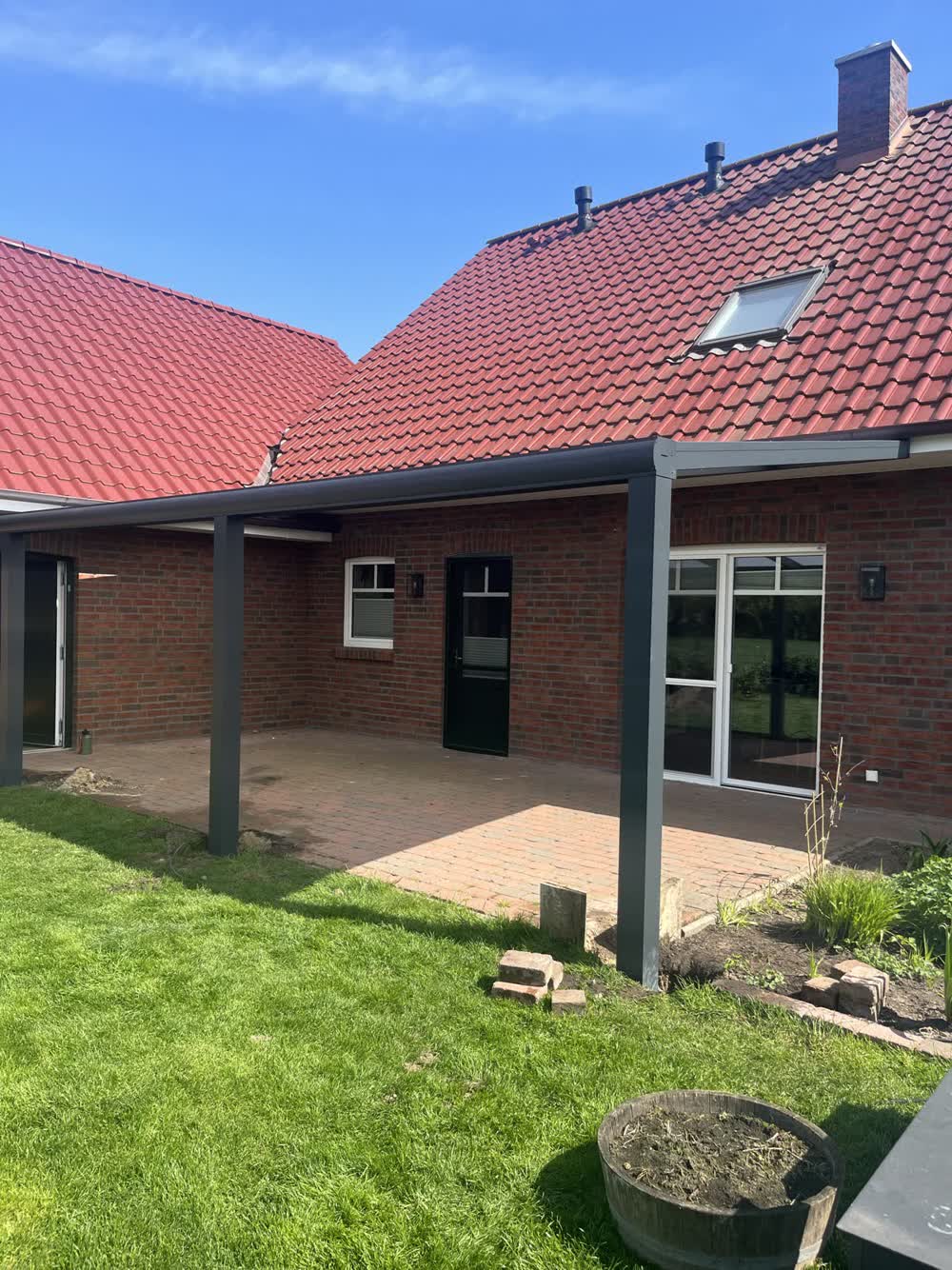 Anthrazitfarbene Basic-Terrassenüberdachung mit opaler Dacheindeckung in der Innenecke eines Klinkerhauses in Osterholte
