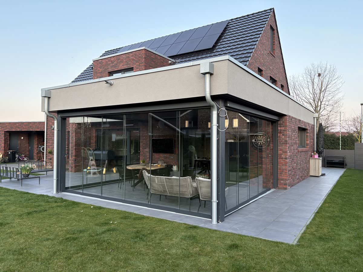 Rahmenlose Glasschiebewände über Eck in einem massiv gebauten Flachdach-Anbau eines Klinkerhauses in Haren