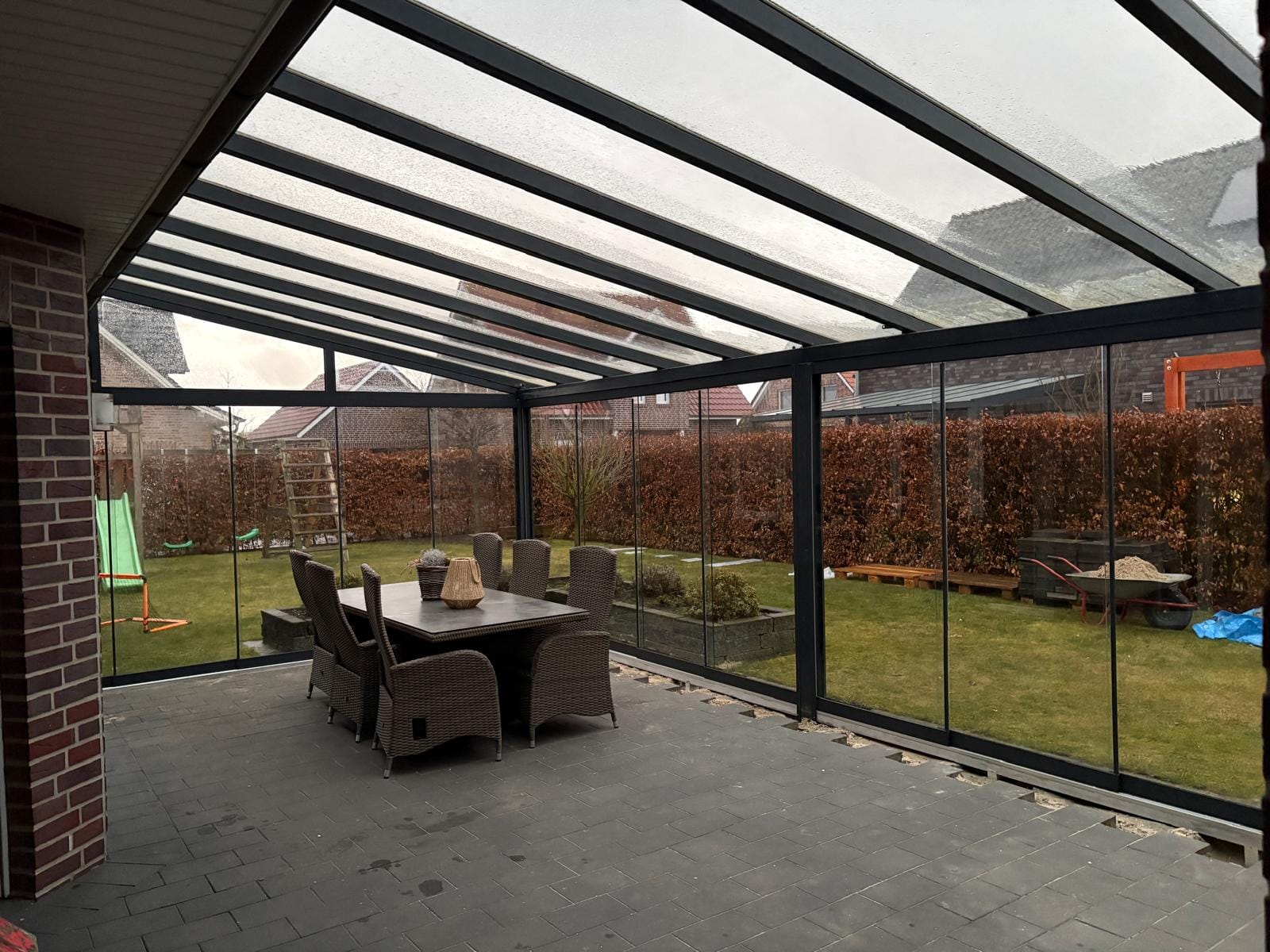 Innenansicht einer mit rahmenlosen Glasschiebewänden geschlossenen Terrasse in Klein Fullen bei Meppen, mit Esstisch und Blick in den winterlichen Garten