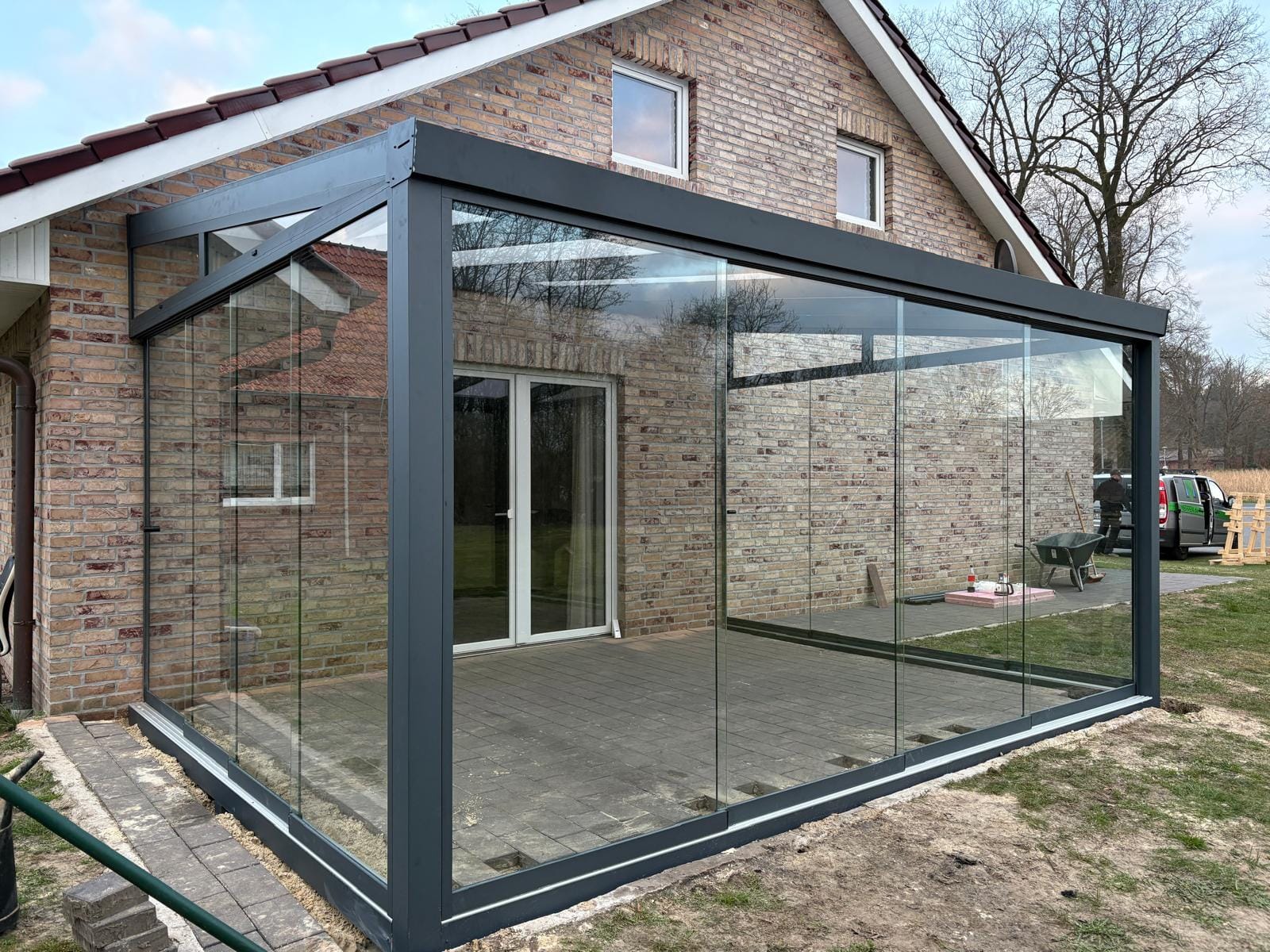 Anthrazitfarbener Kaltwintergarten mit rahmenlosen Glasschiebewänden über Eck an der Giebelseite eines Klinkerhauses in Sögel, aufgenommen im Winter
