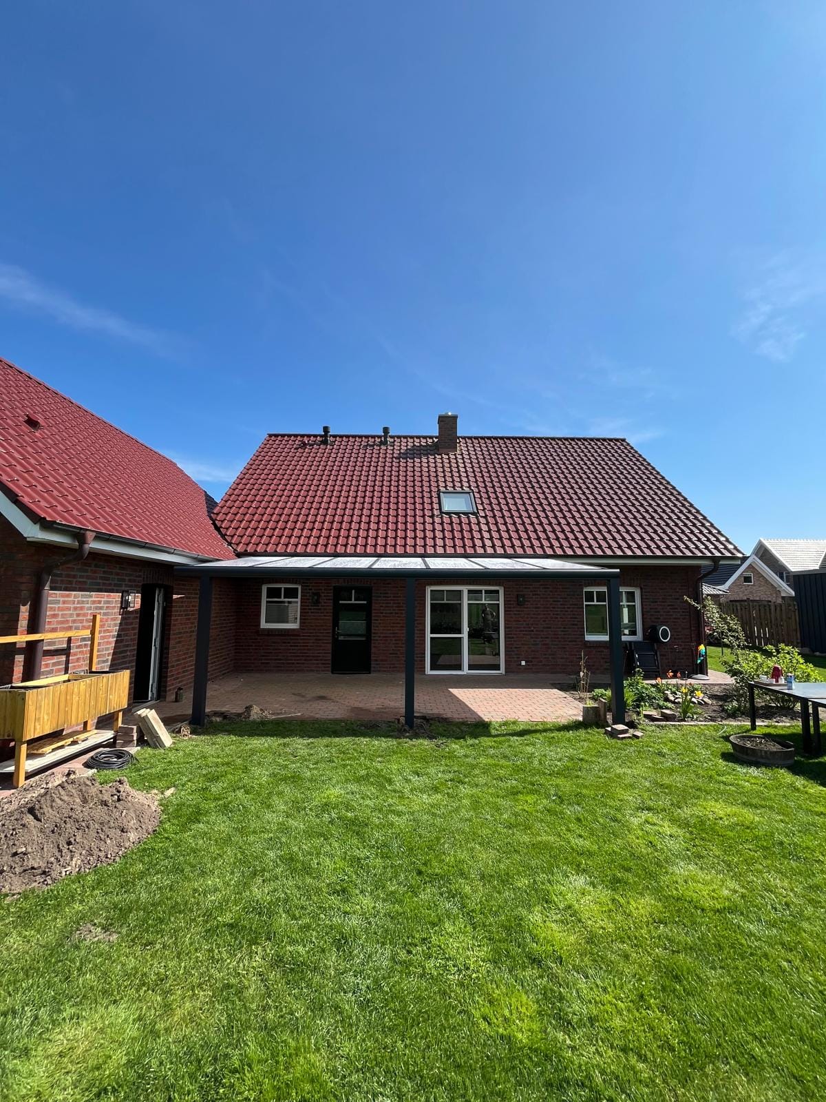 Anthrazitfarbene Premium-Terrassenüberdachung an einem roten Klinkerhaus mit rotem Ziegeldach in Bevern, davor Klinkerpflaster und Rasen