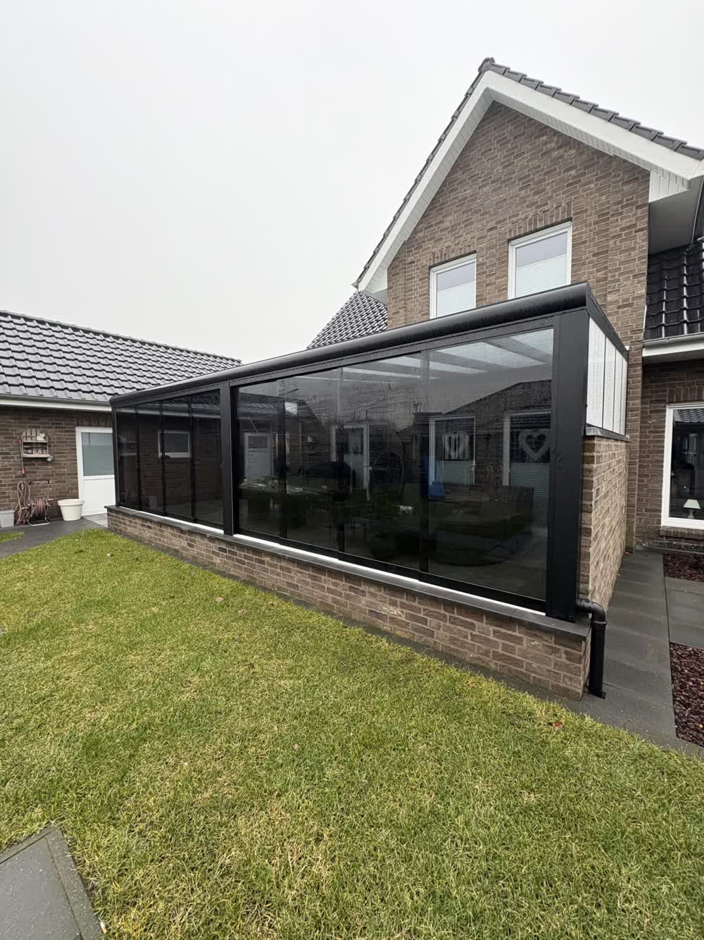 Langer Kaltwintergarten mit getönten Glasschiebewänden auf einem gemauerten Klinkersockel